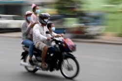 FILE - Members of a family wear face masks, as a preventive measure against the spread of the COVID-19 novel coronavirus, as they ride their motorcycle along a street in Phnom Penh on April 28, 2020.