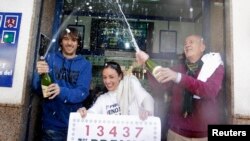 Lottery seller Raquel Carrasco (C) holds a sign with the winning number of Spain's Christmas Lottery "El Gordo", as employees spray champagne in La Eliana near Valencia December 22, 2014. The total prize money of 2.4 billion euros is split into thousands
