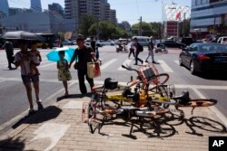 FILE - People walk past bikes from bike-sharing companies thrown in a pile at a traffic junction in Beijing, China, Aug. 4, 2017.