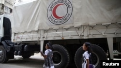 FILE - Two girls walk near a Red Crescent aid convoy carrying urgent medical supplies in the town of Douma, near Damascus, Syria, May 26, 2016.