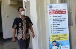 Seorang staf UGM melintas di depan poster terkait Virus Corona di kampus tersebut. (Foto:VOA/ Nurhadi)