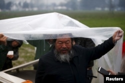 Chinese dissident artist Ai Weiwei speaks to reporters as he holds a rain cover to protect Syrian musician Nour Alkhzam from the rain, after her performance in a field near a makeshift camp on the Greek-Macedonian border, near the village of Idomeni, Gree