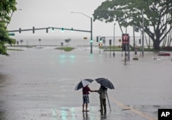 In this Aug. 23, 2018 file photo, people stand near flood waters from Hurricane Lane in Hilo, Hawaii. Some of Hawaii's most iconic beaches could soon be underwater. (Hollyn Johnson/Hawaii Tribune-Herald via AP, File)