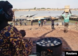 FILE - A Malian woman looks at men carrying humanitarian food aid, Mopti, Mali, Feb. 4, 2013.