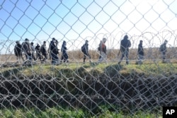 FILE - Migrants walk behind a temporary protective fence at the border between Hungary and Serbia near Morahalom, southeast of Budapest, Hungary, Feb. 22, 2016.