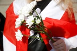 A woman holding flowers and wrapped in the historical white-red-white flag of Belarus attends an action in support of the Belarusian opposition in Warsaw, Poland on September 9, 2020.