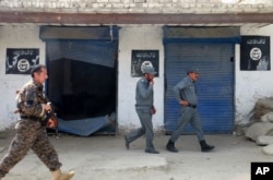 FILE - Afghan police walk past Islamic State militant flags on a wall, after an operation in the Kot district of Jalalabad province east of Kabul, Afghanistan, Aug. 1, 2016.