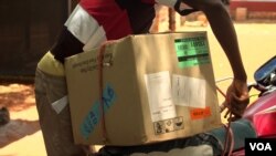 An HIV-positive man loads a box of antiretroviral drugs onto his motorcycle to take back to his village in the Central African Republic. It's a six-month supply for 30 people. (Z. Baddorf/VOA)