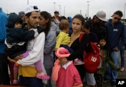 FILE - Venezuelan migrants Jorge Gonzales and his wife Kenia, carrying their boys, wait in line for breakfast, after crossing the border into Peru before the deadline on new regulations that demand passports from migrants in Tumbes, Peru, Aug. 24, 2018.