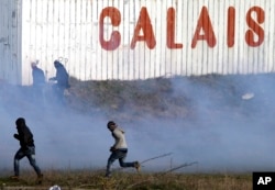 Migrants run away from tear gas thrown by police forces near the Channel Tunnel in Calais, northern France, Jan.21, 2016