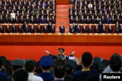 FILE - A conductor leads an orchestra as delegates stand for the national anthem during the closing session of the 19th National Congress of the Communist Party of China at the Great Hall of the People in Beijing, Oct. 24, 2017.