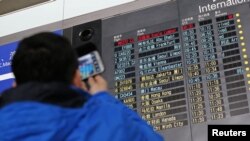 Seorang pengunjung memotret papan informasi jadwal kedatangan pesawat Malaysia Airlines dengan nomor penerbangan MH370 (atas, berwarna merah) di Bandara Internasional Beijing, 8 Maret 2014.