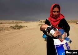 A displaced woman who is fleeing from clashes holds her baby in Qayyarah, during an operation to attack Islamic State militants in Mosul, Iraq, Oct. 19, 2016.