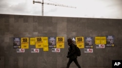 A man walks past posters for the upcoming Catalan regional election in Barcelona, Spain, Monday, Dec. 18, 2017. The Catalan regional government was removed from office by Spain's national government in late October after regional lawmakers passed a declaration of independence that Spanish authorities deemed illegal.