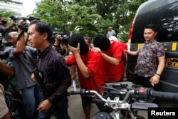 FILE - A plainclothes policeman holds a rifle as he escorts suspects during a police investigation into a men's club after a weekend raid on what authorities described as a "gay spa" in Jakarta, Indonesia, Oct. 9, 2017.