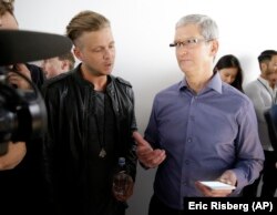 Apple CEO Tim Cook, right, looks at the new iPhone 6s with the members of OneRepublic, in the demo room after Apple event at the Bill Graham Civic Auditorium in San Francisco, Wednesday, Sept. 9, 2015.