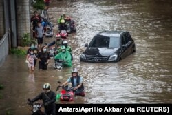 Warga mendorong sepeda motornya melewati air di daerah terdampak banjir menyusul hujan deras di Jakarta, 20 Februari 2021. (Foto: Antara/Aprillio Akbar via REUTERS)
