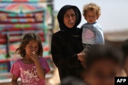FILE - A woman who fled her village in Syria's Idlib province carries a child at a camp in Kafr Lusin near Syria's border with Turkey, Sept. 9, 2018.