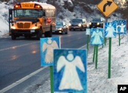 FILE - In this Jan. 3, 2013, file photo, a bus traveling from Newtown, Conn., to Monroe stops near 26 angel signs posted along the roadside in Monroe, Conn., on the first day of classes for Sandy Hook Elementary School students since the December 2012 shooting.