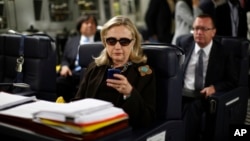 FILE - In this Oct. 18, 2011, file photo, then-Secretary of State Hillary Rodham Clinton checks her Blackberry from a desk inside a C-17 military plane upon her departure from Malta, in the Mediterranean Sea, bound for Tripoli, Libya.
