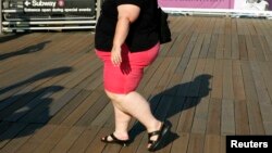 FILE - A woman walks along a boardwalk in New York. The WHO recommends people keep their sugar intake at below 10 percent of their total energy needs.