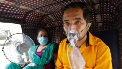 A patient wearing an oxygen mask looks on as his wife holds a battery-operated fan while waiting inside an auto-rickshaw to enter a COVID-19 hospital for treatment, amidst the spread of the coronavirus disease (COVID-19) in Ahmedabad, India, April 25, 2021. (Reuters)