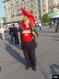 2012年5月普京再次就职总统前夕莫斯科爆发大规模反政府和反普京再次执政示威。一名示威者手举共产党红旗，身穿苏联标志服装表达他对苏联的怀恋。（美国之音白桦拍摄）
