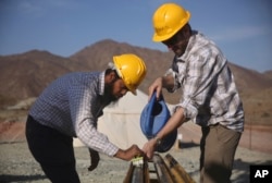 In this March 1, 2017 photo, Nahal Warsi, left, and French geologist Romain Lafay, wash a rock core sample with a brush and water during a geological research project in the al-Hajjar mountains of Oman.