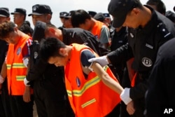 រូបឯកសារ៖ ជនជាតិចិនក្នុង​ឯកសណ្ឋានអាវពណ៌ទឹកក្រូច ត្រូវបានចាប់ខ្លួន​ និង​បញ្ជូន​ទៅ​ប្រទេសចិនវិញ ដោយ​មន្ត្រីប៉ូលិសចិន មុនពេលពួកគេឡើងយន្តហោះចេញពីអាកាសយានដ្ឋានអន្តរជាតិភ្នំពេញនៃប្រទេសកម្ពុជា កាលពីថ្ងៃទី១២ ខែតុលា ឆ្នាំ២០១៧។