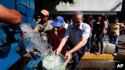 People collect water from a truck that delivers water during rolling blackouts, in Caracas, Venezuela, March 12, 2019.