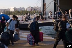 Refugees and migrants carry their belongings after they disembark from a ferry, at the Greece port of Piraeus, near Athens, Sept. 25, 2018. About 400 migrants and refugees arrived at the port from the island of Lesbos.