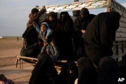 Women and children exit the back of a truck, part of a convoy evacuating hundreds out of the last territory held by Islamic State militants, in the desert near Baghuz, eastern Syria, Feb. 22, 2019.
