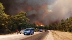 Paramilitary police officers and people watch as a wildfire strengthened by winds spread near the Mediterranean coastal town of Manavgat, Antalya, July 28, 2021. (AP Photo)
