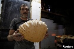 A man poses with a loaf of bread inside a government bakery in Damascus, Syria, Sept. 17, 2016.