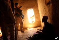 FILE - A U.S. Army soldier and an Afghan translator interrogate a person in the Bagh village of Khakeran Valley, Zabul province, Afghanistan, June 2005. Americans are for the first time targeted by the ICC for possible abuses in Afghanistan.