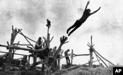 FILE - Rock music fans sit on a tree sculpture as one leaps onto a pile of hay during the Woodstock Music and Art Festival held on a cow pasture at White Lake in Bethel, New York, Aug. 15, 1969.