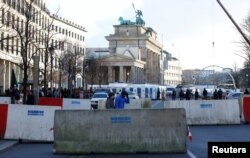 FILE - People walk beside concrete barriers at the Brandenburg Gate, ahead of the upcoming New Year's Eve celebrations in Berlin, Dec. 27, 2016.