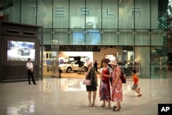 2018年7月5日，一些女士在北京一家高档购物中心的特斯拉展厅外观看智能手机。