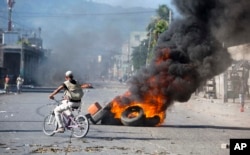 A man rides a bicycle past burning tires set by protesters demanding to know how Petro Caribe funds have been used by the current and past administrations, in Port-au-Prince, Haiti, Oct. 17, 2018.