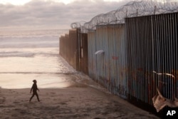 FILE - A woman walks on the beach, Jan. 9, 2019, next to the border wall topped with razor wire in Tijuana, Mexico.