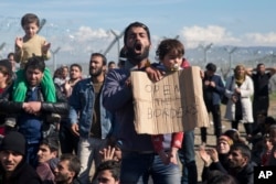 FILE - Stranded refugees and migrants protest in front of the wire fence that separates the Greek side from the Macedonian one at the northern Greek border station of Idomeni, Feb. 27, 2016.