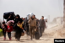 People walk with their belongings as they flee the rebel-held town of Hammouriyeh, in the village of Beit Sawa, eastern Ghouta, Syria, March 15, 2018.