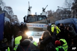 Demonstrators sit in front of a police water cannon on the Champs-Elysees, Dec. 15, 2018, in Paris. It was the fifth straight weekend of protests by the "yellow vest" movement against France's high cost of living.