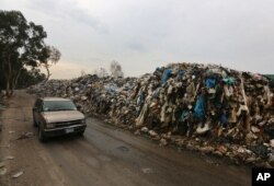 FILE - A car passes by a pile of garbage in Karantina, east Beirut, Lebanon, Dec. 17, 2015.