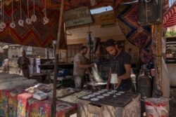 In this May 9, 2020 photo, 28-year-old football defender Mahrous Mahmoud, right, makes Ramadan sweets at a souq, in Manfalut, a town 350 kilometers (230 miles) south of Cairo in the province of Assiut, Egypt. Mahmoud should be on the field at this time of year playing as a defender for Beni Suef, a club in Egypt's second division. But like millions in the Arab world's most populous country, he has been hit hard by the coronavirus pandemic. (AP Photo/Nariman El-Mofty)