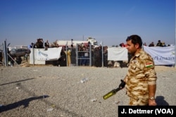 A Kurdish policeman patrols the entrance to the Khasir camp and displaced civilians sure waiting to enter the camp at Khasir.