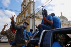 FILE - Armed pro-government militia members flash victory signs as they occupy the Monimbo neighborhood of Masaya, Nicaragua, July 18, 2018.