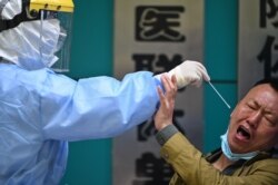 A man being tested for the COVID-19 novel coronavirus reacts as a medical worker takes a swab sample in Wuhan in China's central Hubei province on April 16, 2020.