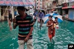 Bangladeshi people walk through a waterlogged street after heavy rainfall in Dhaka, Bangladesh, Saturday, May 21, 2016.
