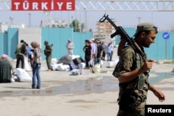 A Kurdish People's Protection Units (YPG) fighter walks near residents who had fled Tel Abyad, as they re-enter Syria from Turkey after the YPG took control of the area, at Tel Abyad town, Raqqa governorate, Syria, June 23, 2015.